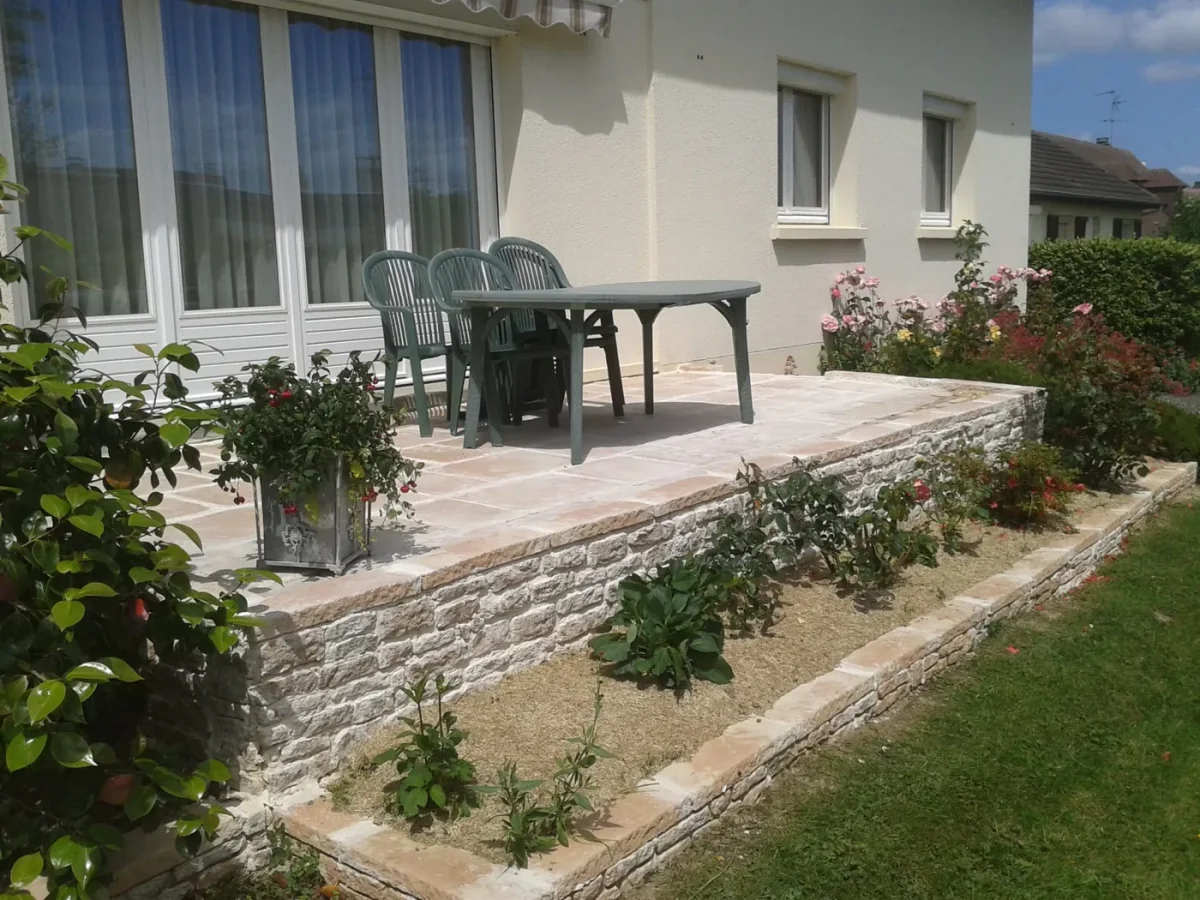 Terrasse en pierre et muret bordé de rosiers devant une maison