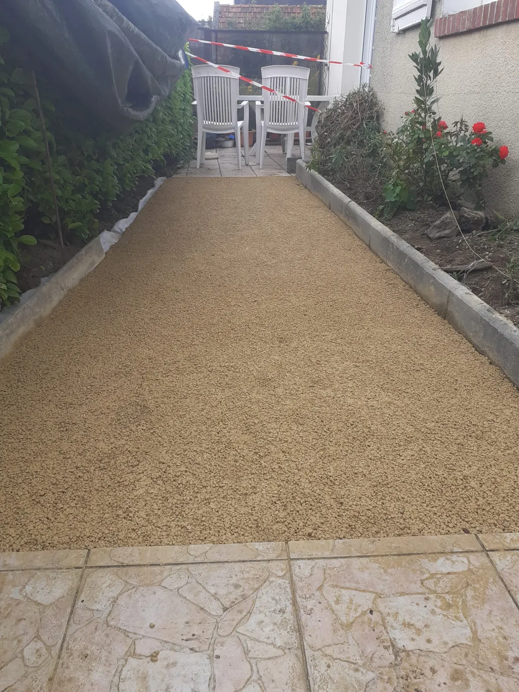 Allée gravillonnée entre deux bordures, le long d'une maison