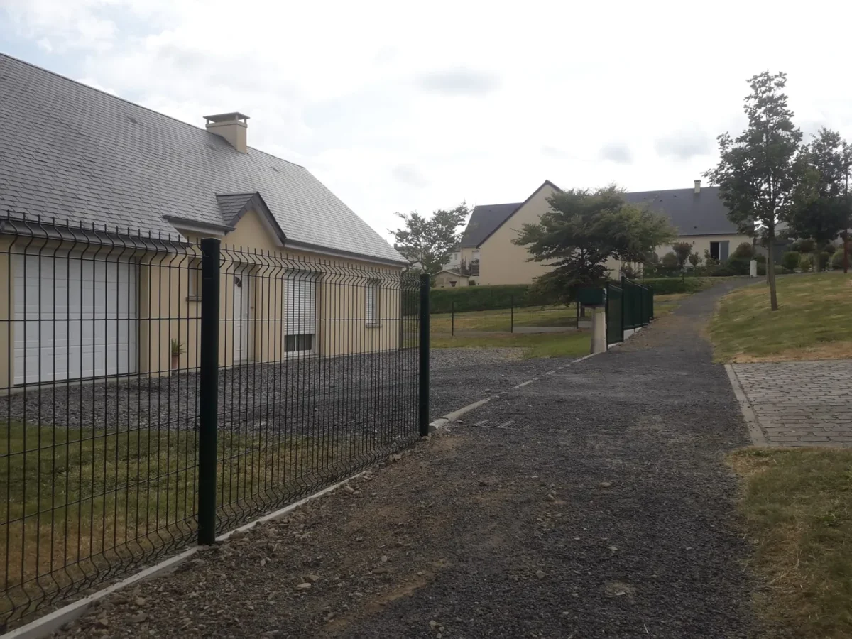 Clôture en grillage rigide vert le long d'une allée gravillonnée, devant une maison